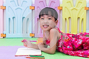 Happy Asian Chinese little girl laying on the floor coloring