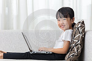 Happy Asian Chinese little girl lying on sofa with laptop