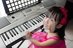 Happy Asian Chinese little girl playing electric piano keyboard