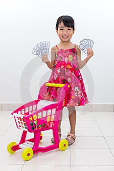 Happy Asian Chinese little girl pushing toy trolley holding cash