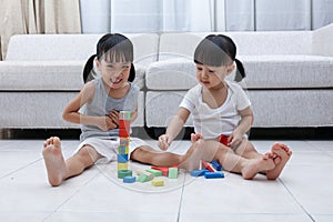 Happy Asian Chinese little sisters playing blocks on the floor