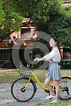 Happy Asian Chinese pretty girl riding a bike wear student suit in school