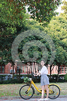 Happy Asian Chinese pretty girl riding a bike wear student suit in school