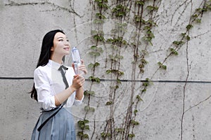 Happy Asian Chinese pretty girl wear student suit in school drinking water in nature in spring