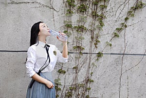 Happy Asian Chinese pretty girl wear student suit in school drinking water in nature in spring