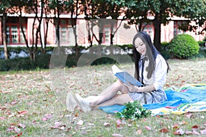 Happy Asian Chinese pretty girl wear student suit in school read book sit on grass