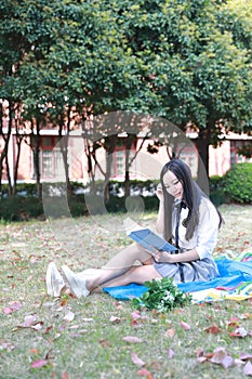 Happy Asian Chinese pretty girl wear student suit in school read book sit on grass