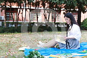 Happy Asian Chinese pretty girl wear student suit in school read book sit on grass