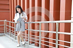 Happy Asian Chinese pretty girl wear student suit in school reading book in nature in spring