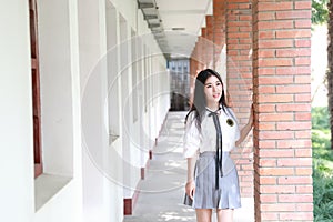 Happy Asian Chinese pretty girl wear student suit in school stand by a wall in nature in spring