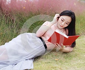 Happy Asian Chinese woman girl lying on grass dream pray flower field autumn fall park lawn hope nature read book knowledge