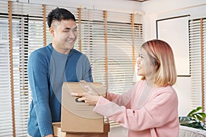 Happy asian couple carry cardboard boxes while moving to new house in living room.unpacking for new home.woman wipe the sweat her