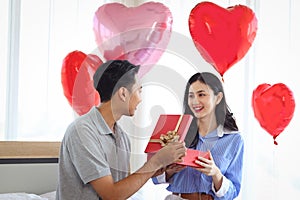Happy Asian couple celebrating anniversary their love together, boyfriend giving red present gift box to surprised girlfriend,