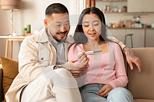 Happy Asian Couple Celebrating Positive Result Of Pregnancy Test Indoor