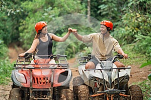 happy asian couple doing highfive while riding atv through the track