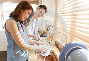 Happy Asian couple family washing dishes together at kitchen after breakfast