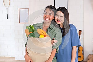 Happy asian couple lesbian holding vegetable bag  looing at camera after shopping at grocery store at home.LGBTQ lifestyle concept photo
