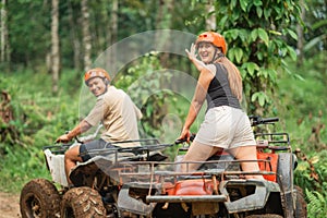 happy asian couple looking back to the camera while riding the atv