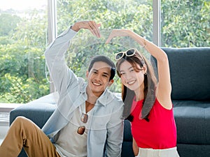 Happy Asian couple lover ready to trip, young woman and man in colorful casual making heart shape by hands.