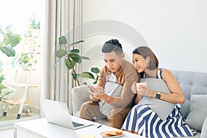 Happy Asian couple lover using mobile, laptop together at home
