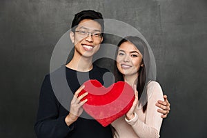 Happy asian couple posing together while holding heart toy