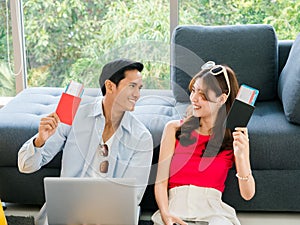 Happy Asian couple ready to trip, young man and woman, holding and showing passport while using laptop computer.