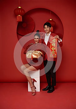 Happy asian couple in red casual attire holding gift box and spring festival couplet bless for Chinese new year day