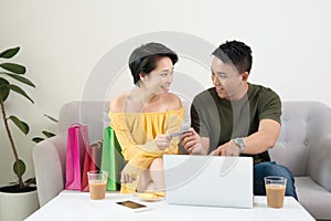 Happy Asian couple shopping online with holding credit card and laptop and sitting at home together, lifestyle concept