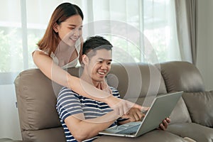 Happy asian couple shopping online using digital tablet with holding credit card and sitting on sofa at home together.