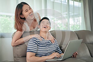 Happy asian couple shopping online using digital tablet with holding credit card and sitting on sofa at home together.