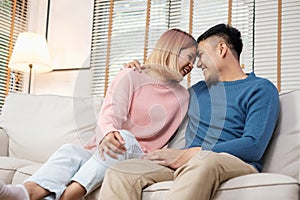 Happy asian couple sitting on sofa after unpacking cardboard boxes  while moving to new home at sofa in living room.new house