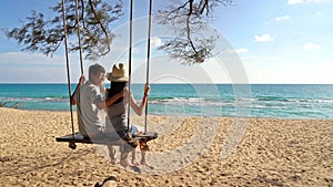 Happy Asian couple swinging on a swing at the beach during travel trip on holidays vacation outdoors at ocean or nature sea at