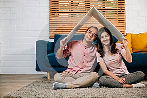 Happy Asian couple in their new apartment assembles cardboard home roof