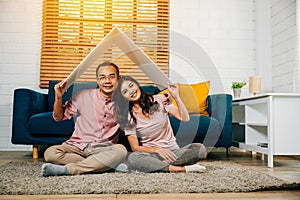 Happy Asian couple in their new apartment assembles cardboard home roof