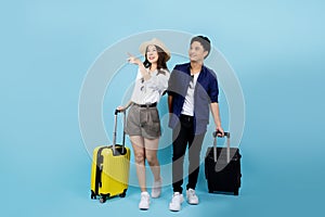 Happy Asian couple tourist hand pointing to copy space with suitcases going to travel on holidays isolated on blue background