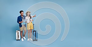 Happy Asian couple tourist looking map and hand pointing to copy space with baggage going to travel on holidays isolated on blue