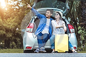 Happy Asian couple traveling and sitting in a car open trunk and watch sunrise.