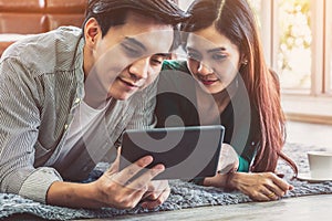 Happy Asian couple use tablet while lying down