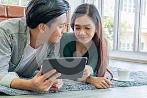 Happy Asian couple use tablet while lying down