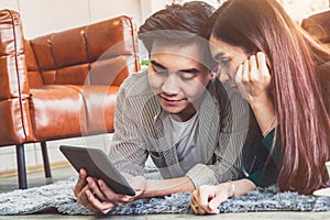 Happy Asian couple use tablet while lying down