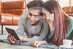 Happy Asian couple use tablet while lying down