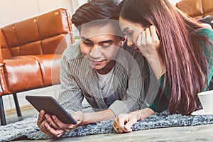 Happy Asian couple use tablet while lying down