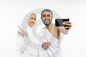 Happy asian couple wearing ihram clothes use smartphone for selfie