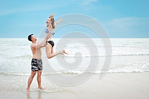 Happy asian couple who wearing blue bikini and black swimming suit throws his girlfriend up while he smiling and laughing on