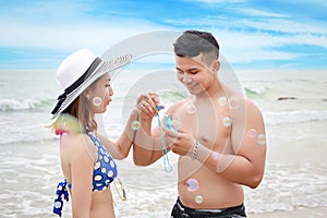 Happy asian couple who wearing blue bikini, white hat and black swimming suit having good time on the beach. they playing with