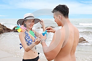 Happy asian couple who wearing blue bikini, white hat and black swimming suit having good time on the beach. they playing with