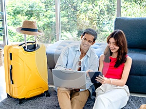 Happy Asian couple, young man and woman looking and using laptop computer and smartphone together.