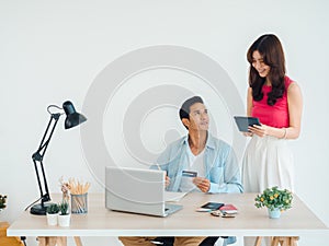Happy Asian couple, young man and woman using tablet and laptop computer together for flight booking.