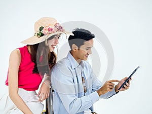 Happy Asian couple, young woman with beach hat and man in denim shirt using tablet together for trip information.