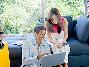 Happy Asian couple, young woman and man looking and using laptop computer and smartphone together.